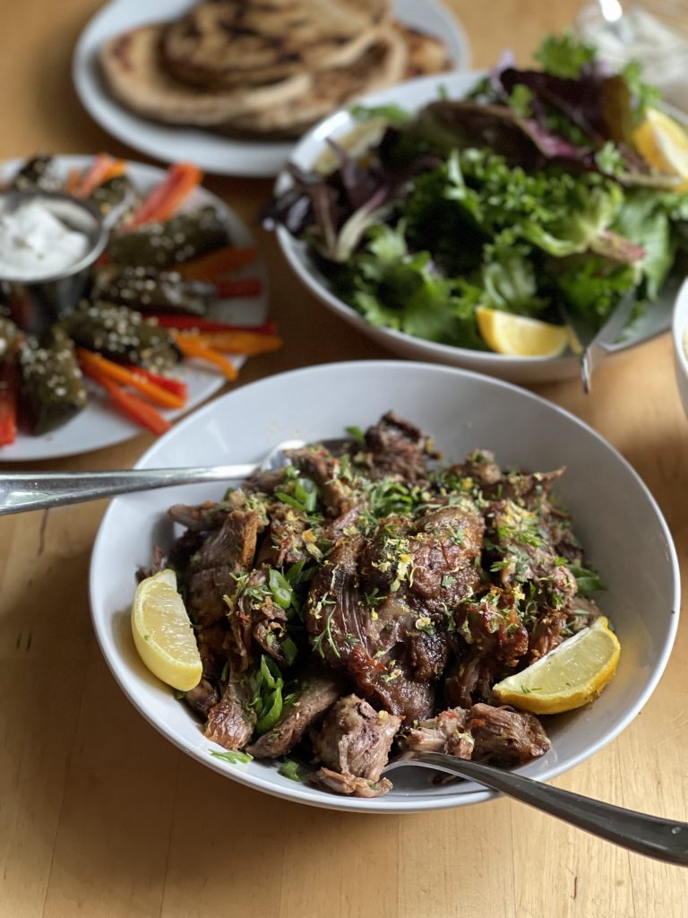 A bowl of tender lamb, garnished with herbs and served with lemon wedges.
