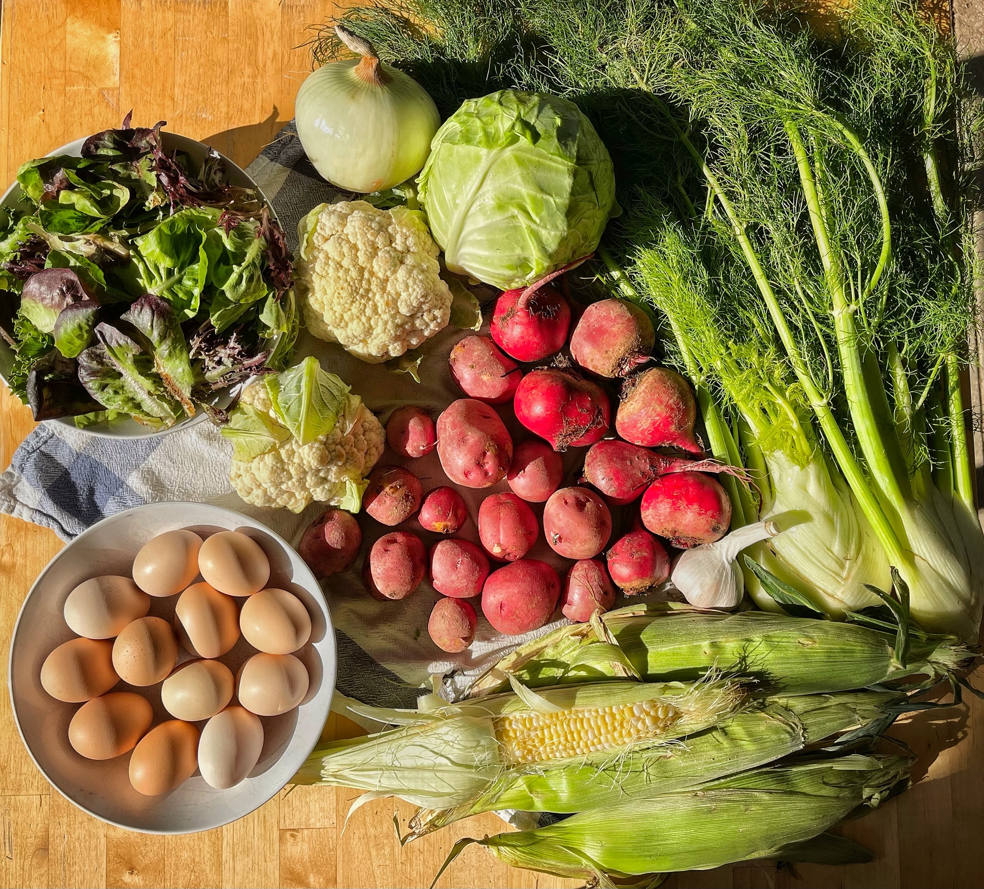 A selection of freshly grown Rootbound vegetables (including red potatoes, cabbage, and fennel) and eggs.