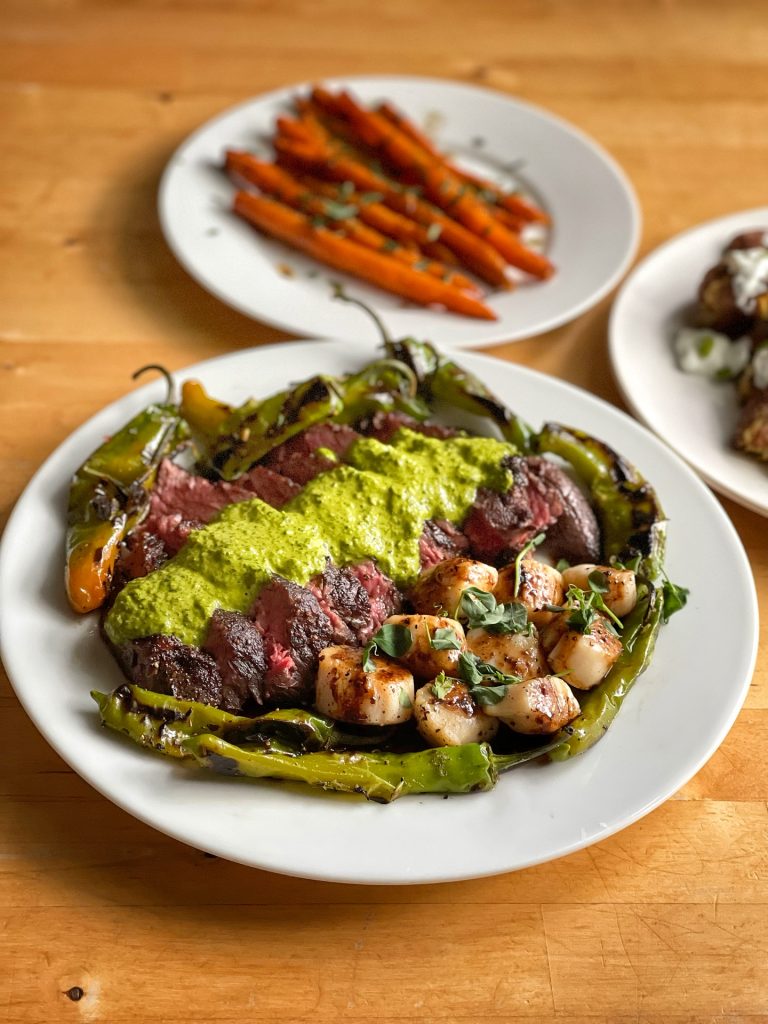 A plate of prepared lamb meat with green sauce and a side of roasted carrots.