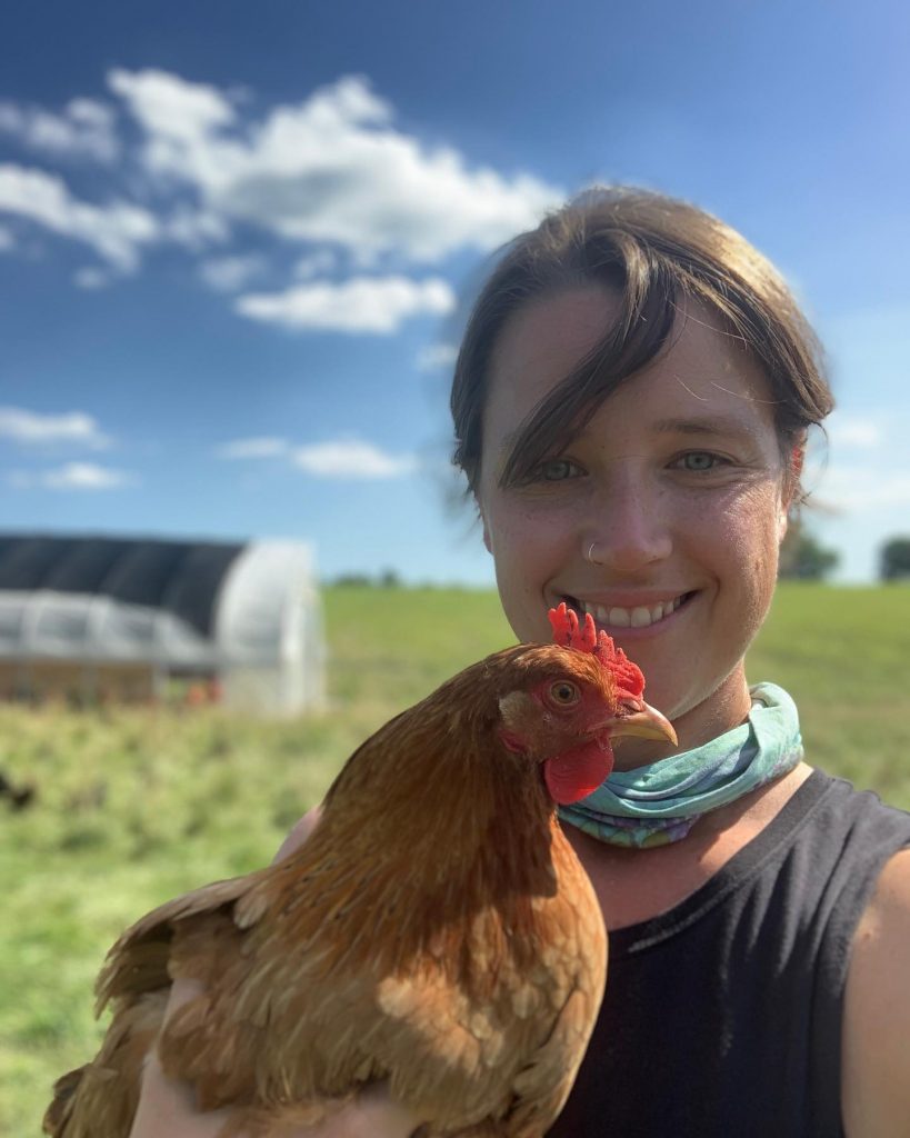 A smiling Rootbound farmer holding a chicken.